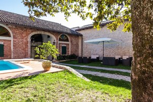 Pátio com piscina, área de estar ao ar livre e edifício de pedra com arcos.