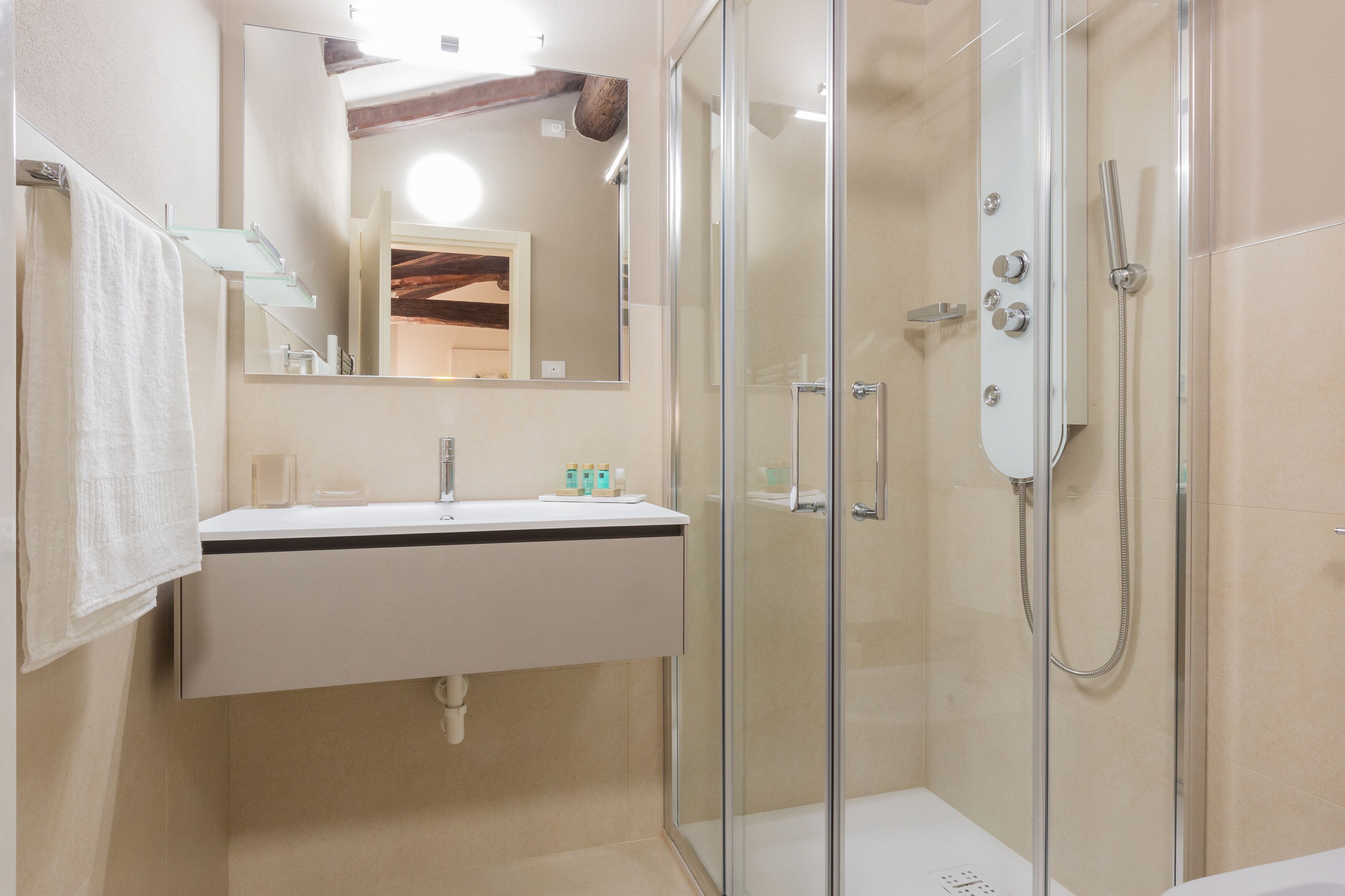 Un baño moderno con ducha de vidrio, un lavamanos blanco con espejo y una toalla colgada en la pared.
