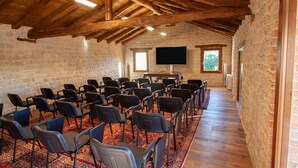Un salón de conferencias con filas de sillas, techo de madera, paredes de piedra y una televisión de pantalla plana.