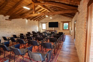 Uma sala de conferências com fileiras de cadeiras, teto de madeira, paredes de pedra e uma televisão de tela plana.