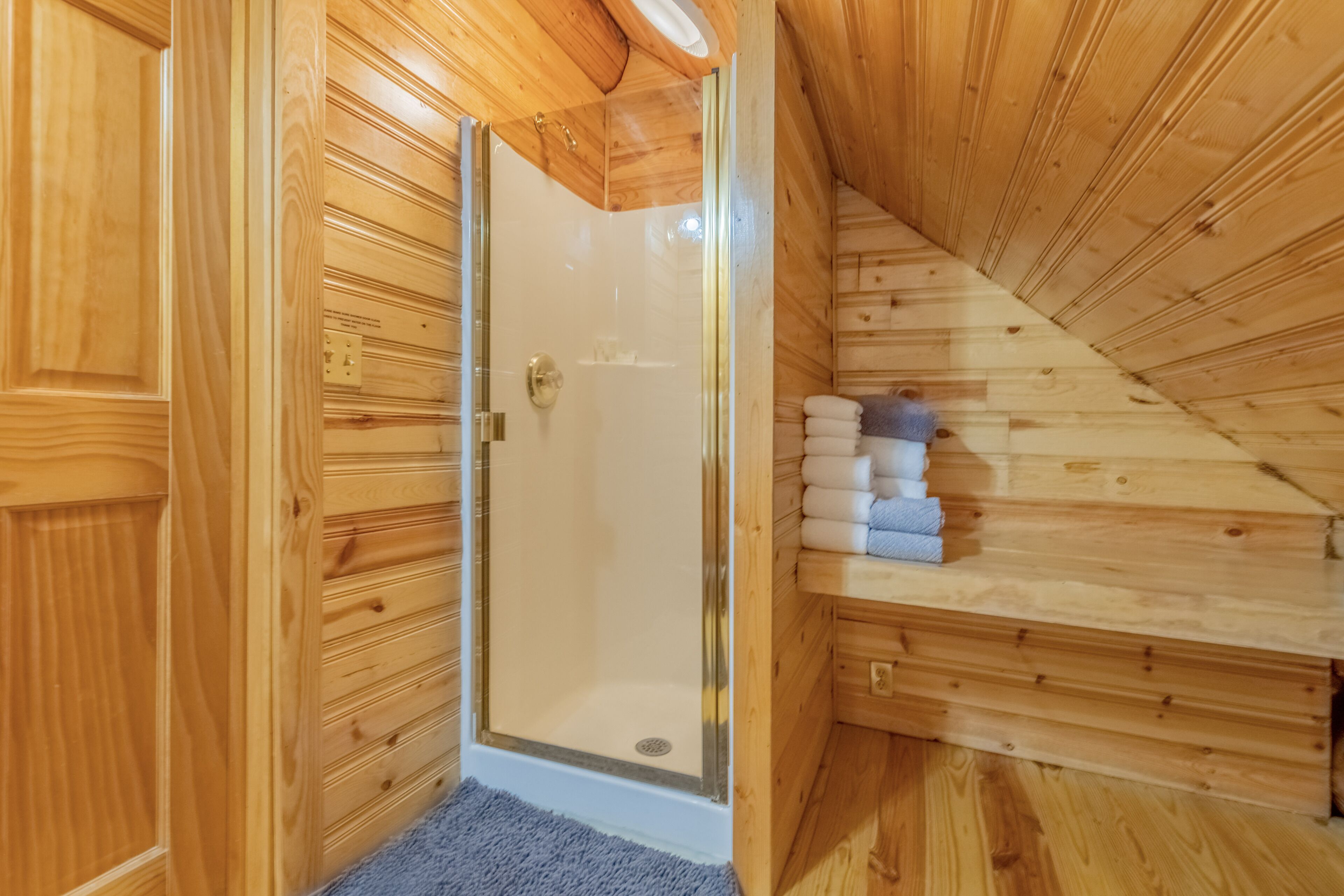 Ein Holzblock-Interieur mit einer glaserne Dusche, Holzwänden und einem Regal mit Handtüchern.