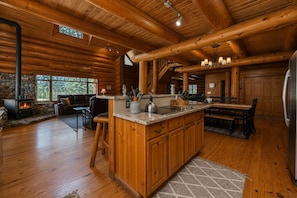 A log cabin interior with a stone fireplace, wooden dining table, and a kitchen area. - Log Cabin Life| Hot Tub | Pool Table | BBQ | Deck (Leavenworth)