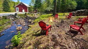 Une cabane rustique avec un foyer et des chaises Adirondack rouges, située dans une zone boisée.
