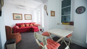 A cozy living room with a red sofa, a white table with chairs, and a window with a view of the sea. - Charming Colonial Flat in historic building (Castle Road)