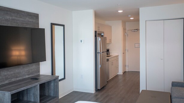 Un apartamento moderno con sala de estar que incluye televisor de pantalla plana y estanterías empotradas, cocina con electrodomésticos de acero inoxidable y comedor independiente.