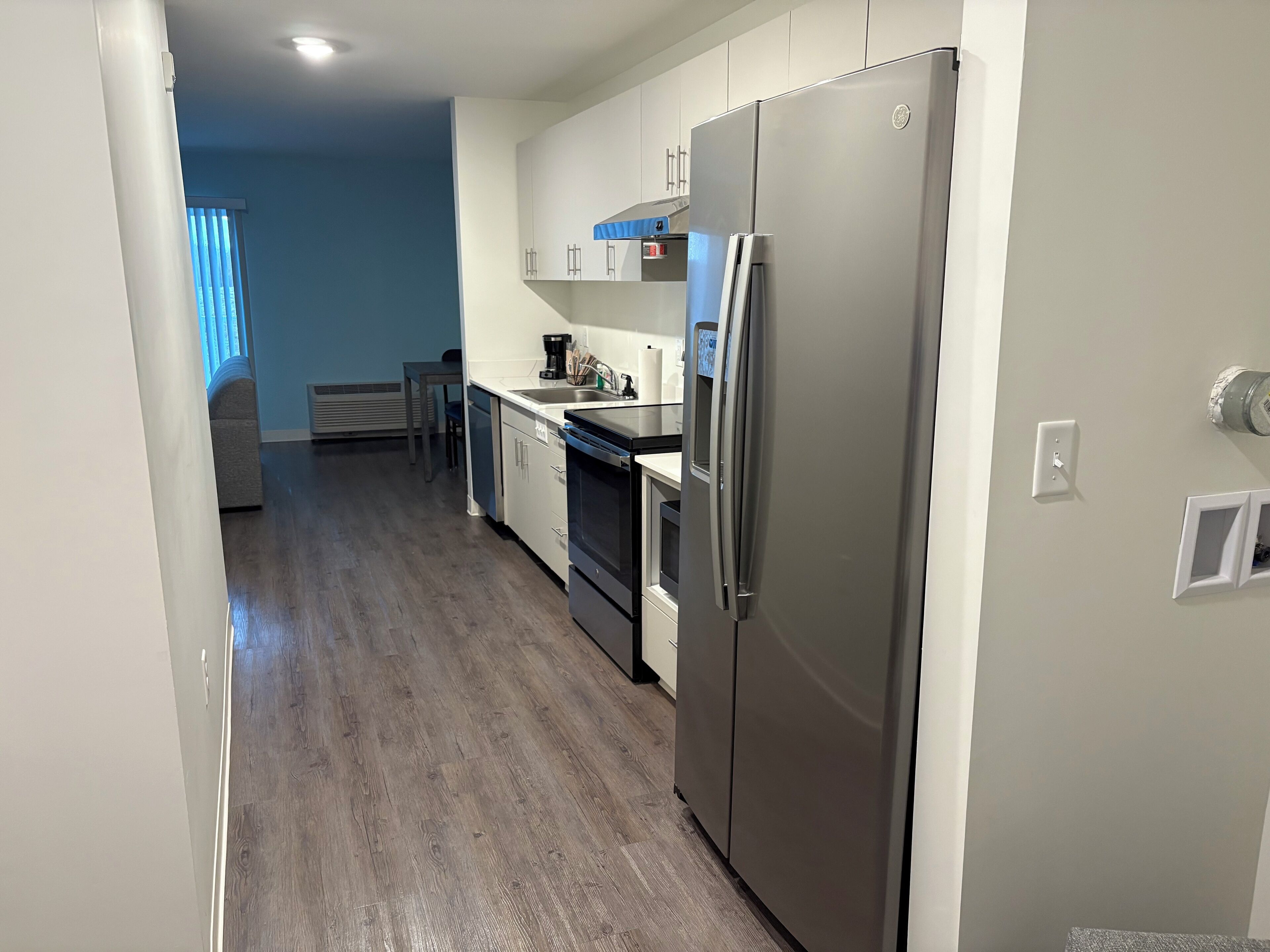 A modern kitchen with a stainless steel refrigerator, white cabinets, and a wooden floor.
