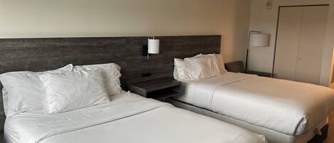 A hotel room with two single beds, a nightstand, a wall-mounted lamp, and a wardrobe.
