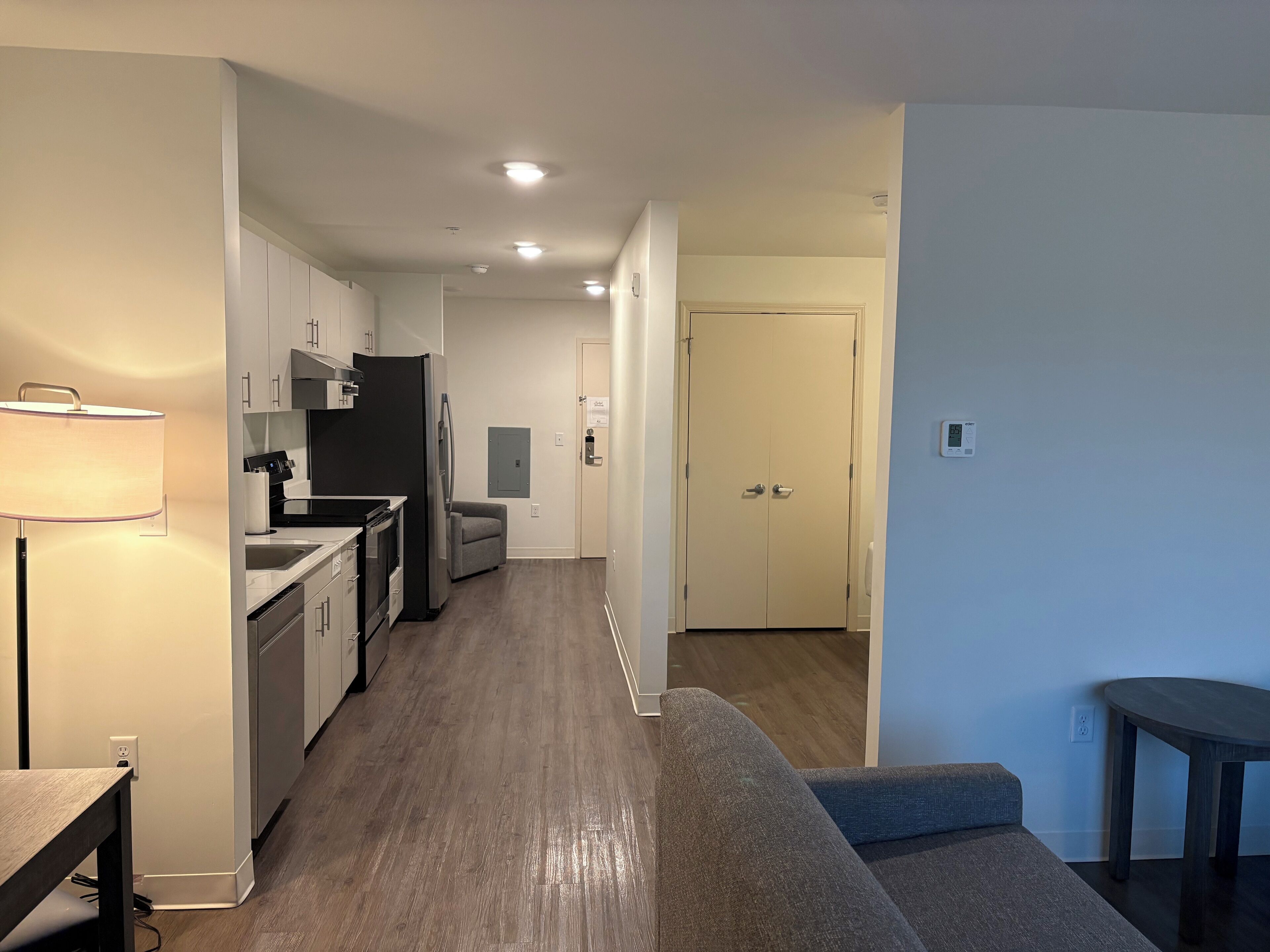 A modern kitchen with white cabinets, a refrigerator, and a dining area with a table and lamp.