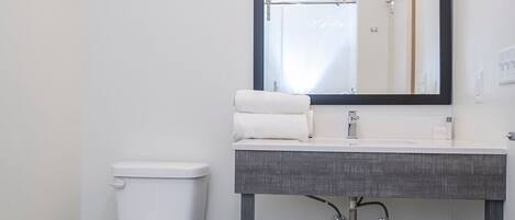 A modern bathroom with a white toilet, a grey vanity with a mirror, and a light fixture above the mirror.