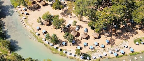 An aerial view of a beach resort with thatched-roof huts and sun loungers arranged in rows along the shoreline.