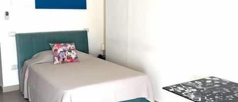 A bedroom with a bed, a table, and a painting on the wall.