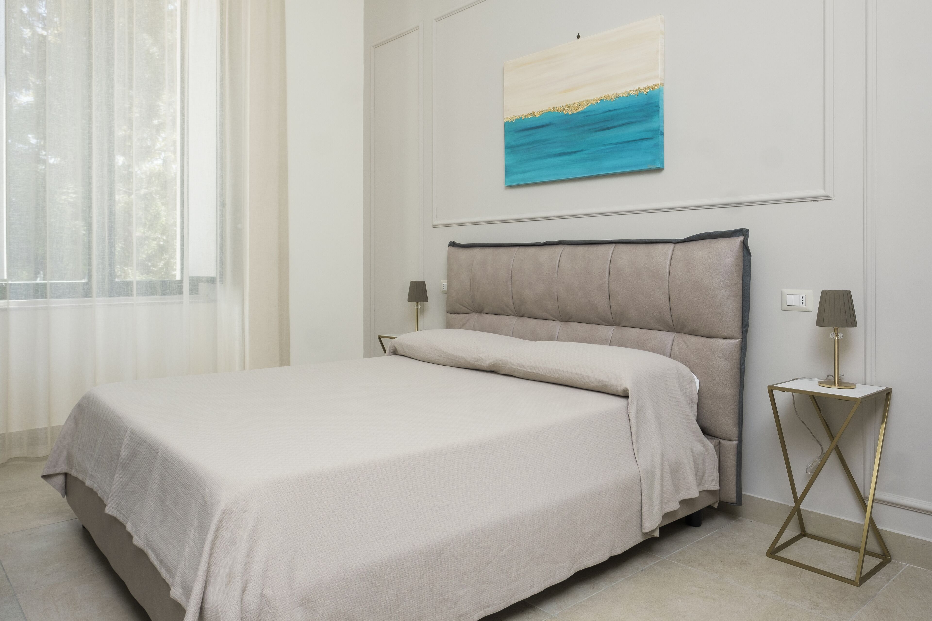 A neatly made bed with a light-colored bedspread, a headboard with a dark trim, and a small bedside table with a lamp.
