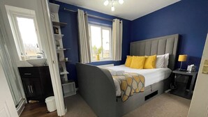 A bedroom with a bed, bedside table, lamp, window, and a bathroom with a sink and toilet.