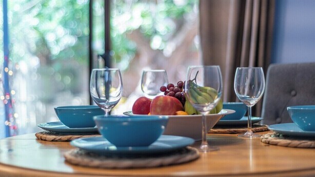 A table set with blue bowls, plates, and wine glasses, with a bowl of fruit and grapes in the center.