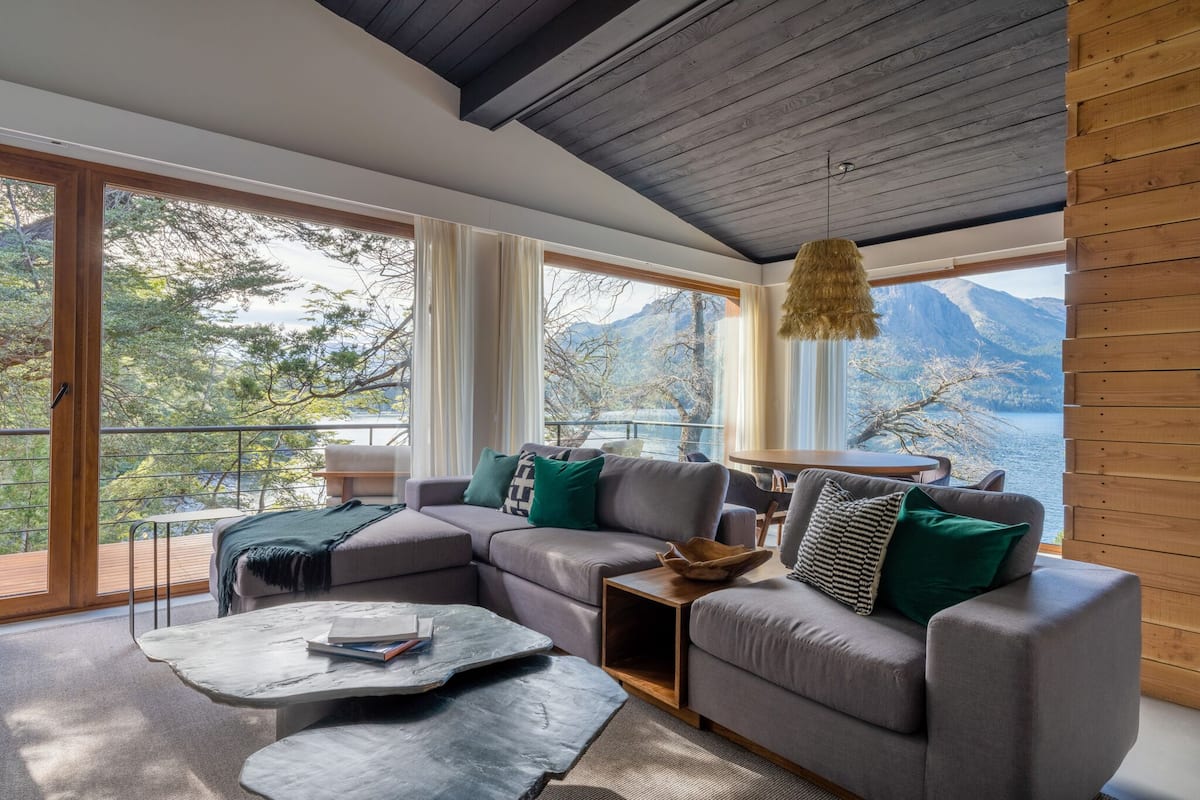 A modern living room with a sectional sofa, a coffee table, and a view of a lake and mountains.