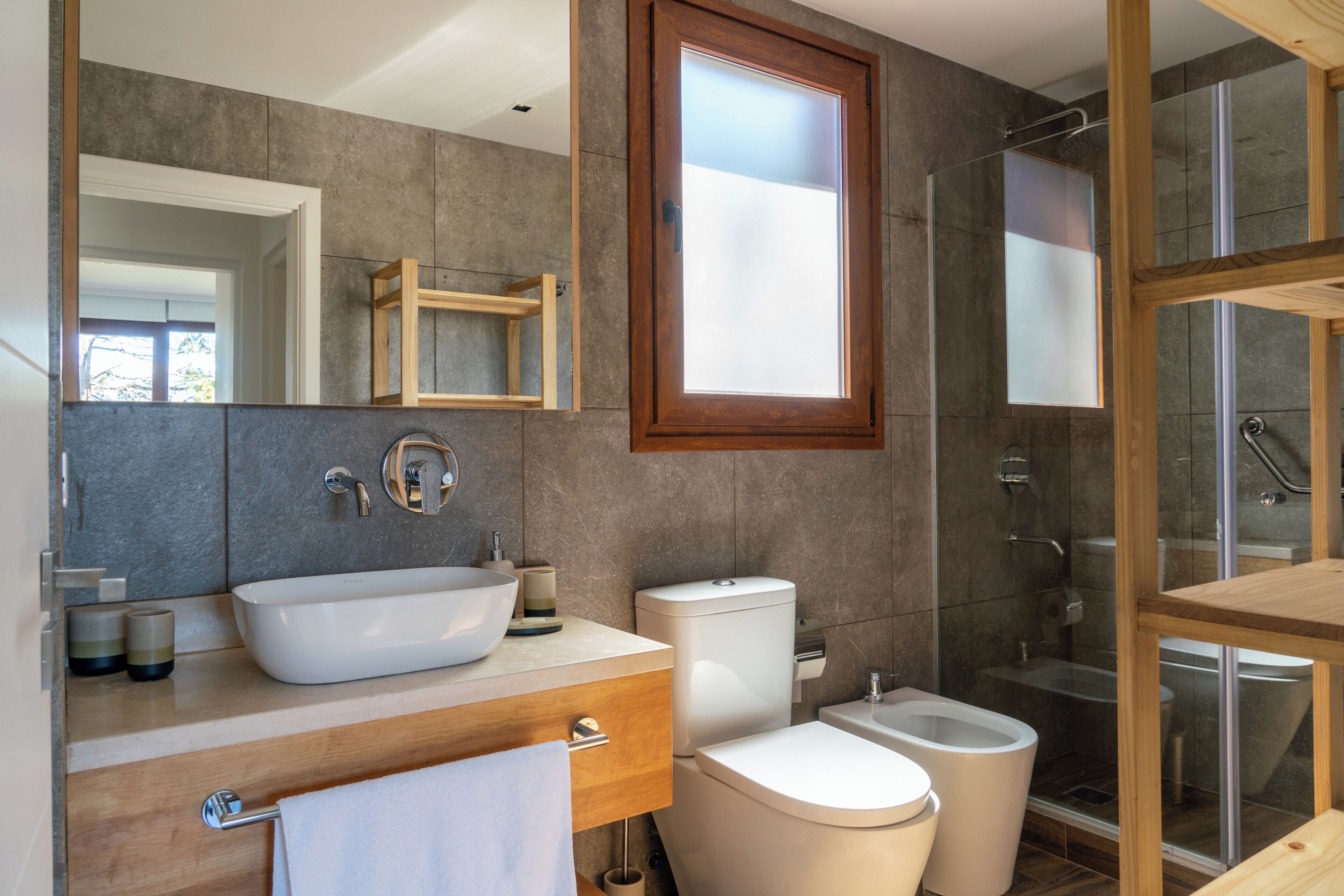Un baño moderno con un espejo grande, un lavabo sobre encimera, un inodoro y una zona de ducha con mampara de cristal.