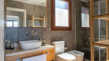 Un baño moderno con un espejo grande, un lavabo sobre encimera, un inodoro y una zona de ducha con mampara de cristal.