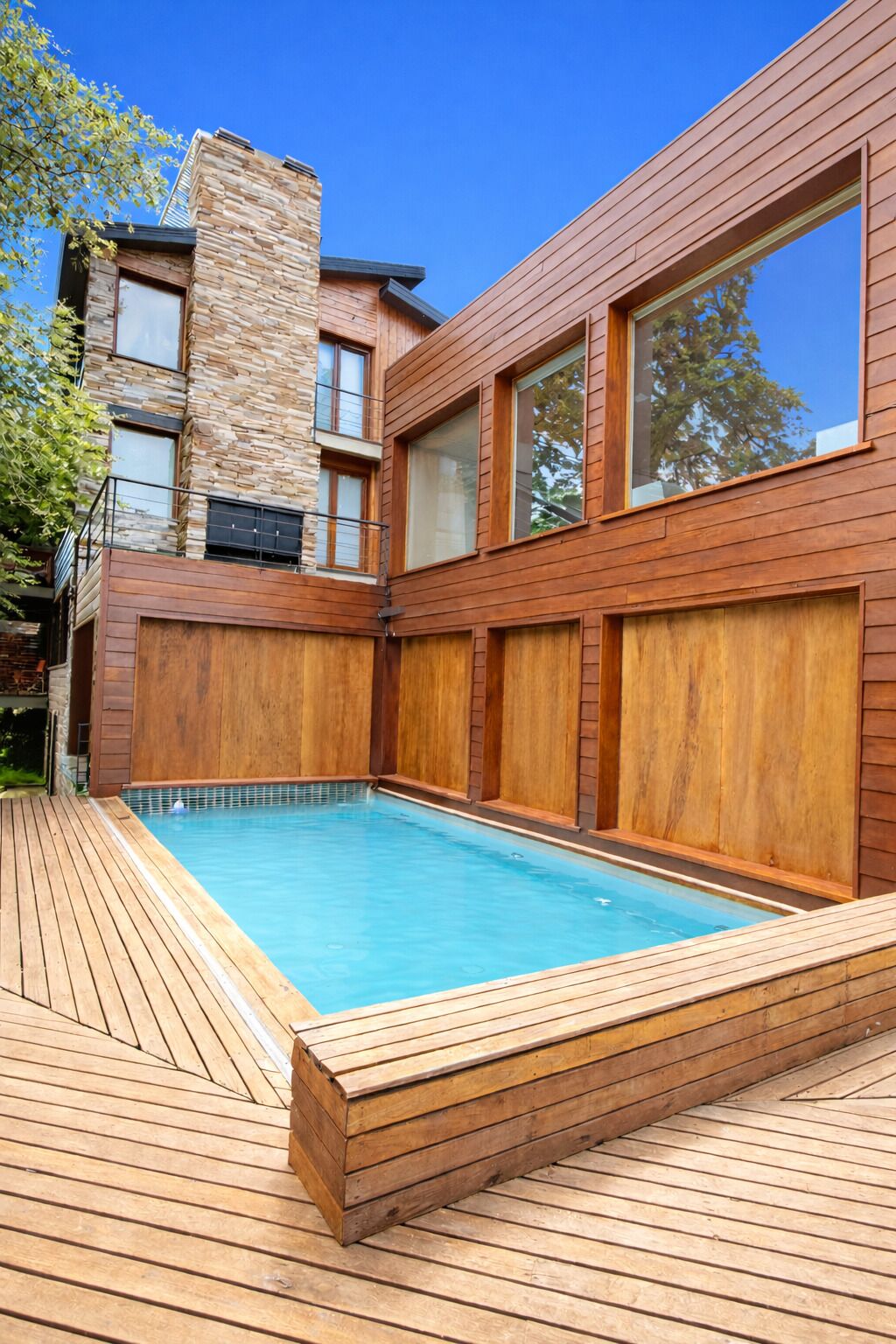 Una casa moderna con piscina, terraza de madera y fachada de piedra.
