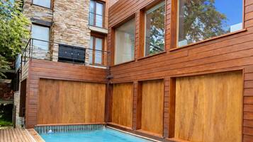 Una casa moderna con piscina, terraza de madera y fachada de piedra.