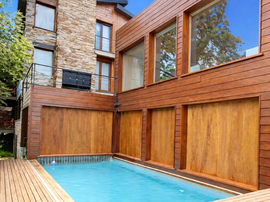 Una casa moderna con piscina, terraza de madera y fachada de piedra.