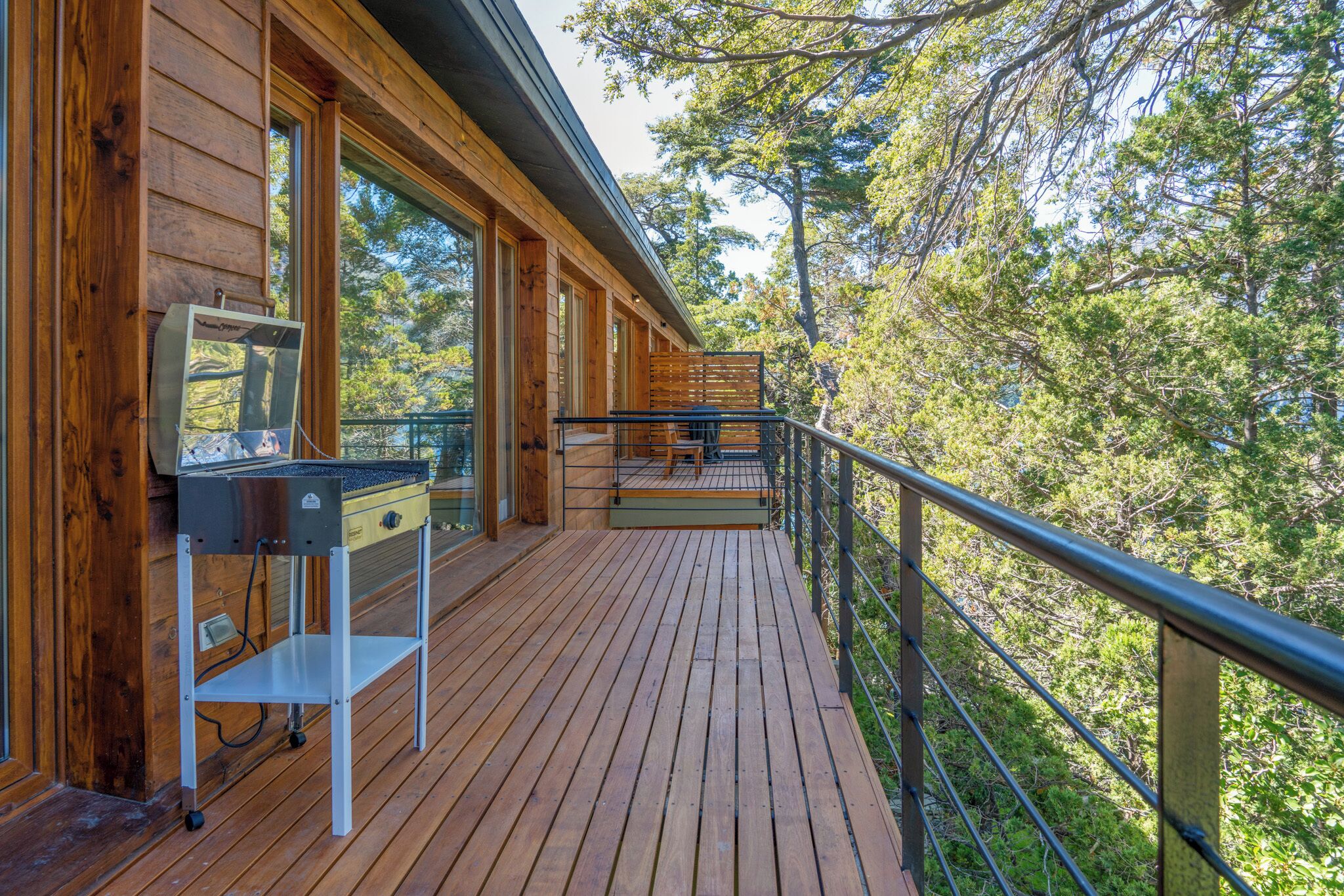 A wooden deck with a grill and a small table, overlooking a forested area.