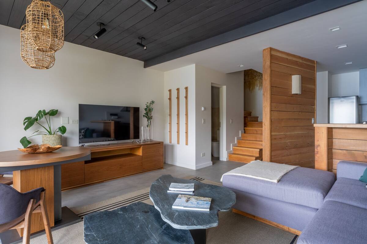 A modern living room with a television, wooden furniture, a staircase, and a kitchen area.