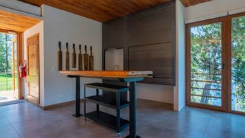 A modern kitchen with a wooden table, black metal shelves, and a large window with a view of trees.