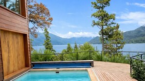 Una piscina con cubierta de madera, rodeada de árboles y vistas a un lago y montañas.