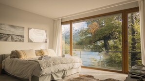 Un dormitorio con una cama grande, vistas a un lago y suelo de madera.