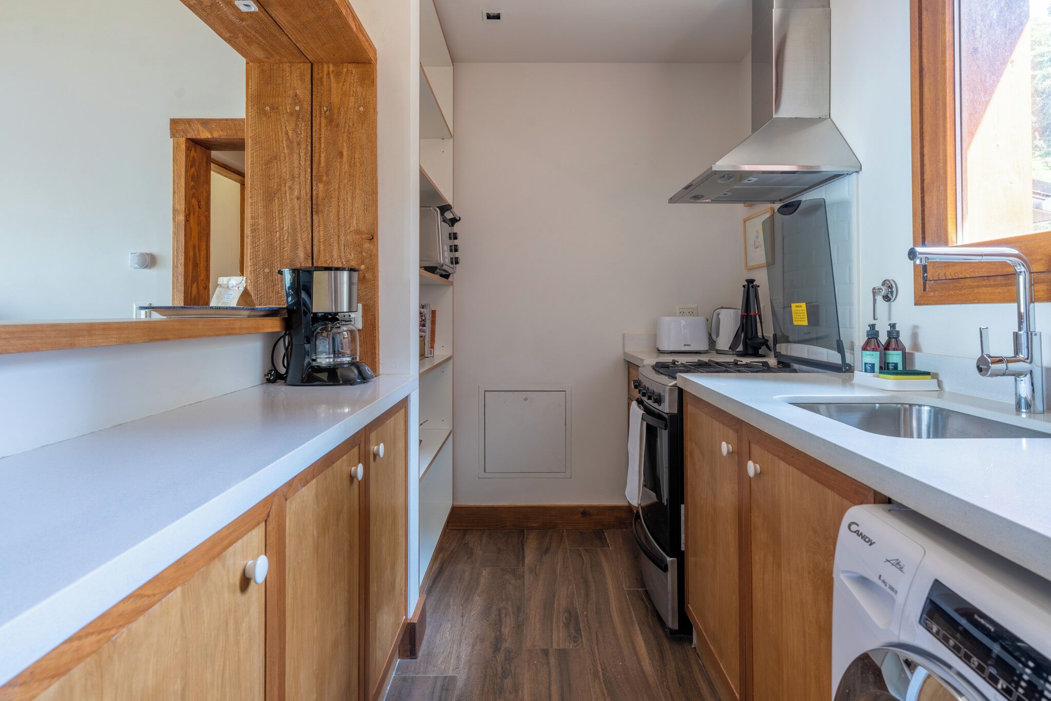 Una cocina compacta con armarios de madera, horno empotrado, cafetera y lavavajillas.