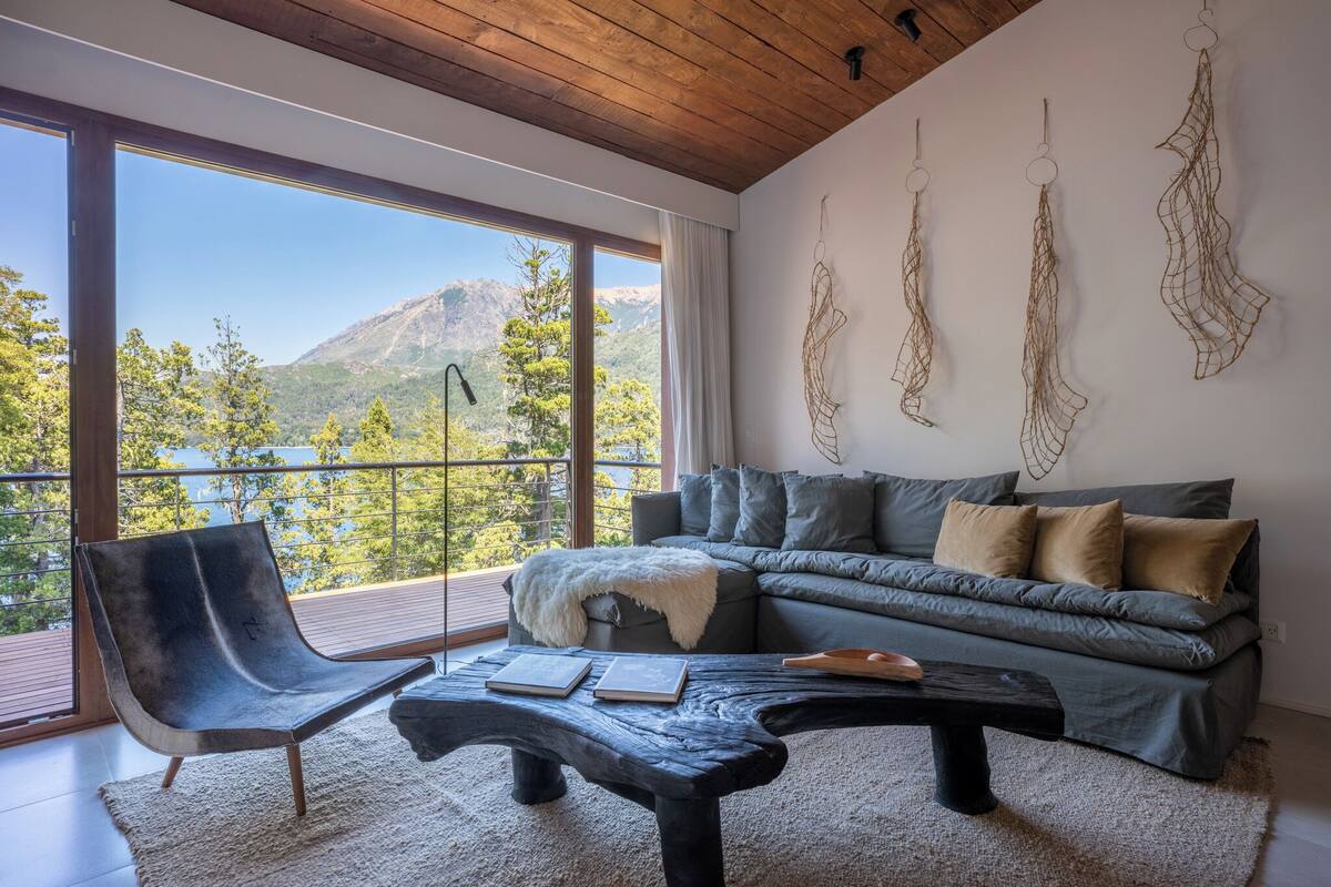 A modern living room with a large window, a grey sofa, a black chair, and a coffee table.
