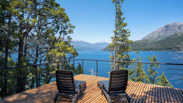 Terraza de madera con dos sillones de descanso con vistas a un lago y montañas.