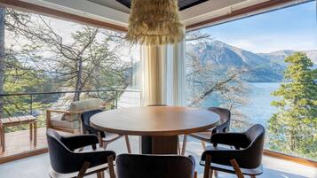 Ein Essbereich mit einem runden Tisch und vier Stühlen, der auf eine Berglandschaft und ein Gewässer blickt.