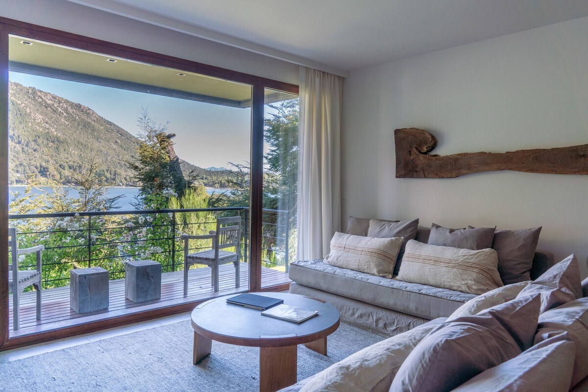 Una sala de estar moderna con un amplio ventanal corredera que da a un balcón con vistas panorámicas a la montaña.
