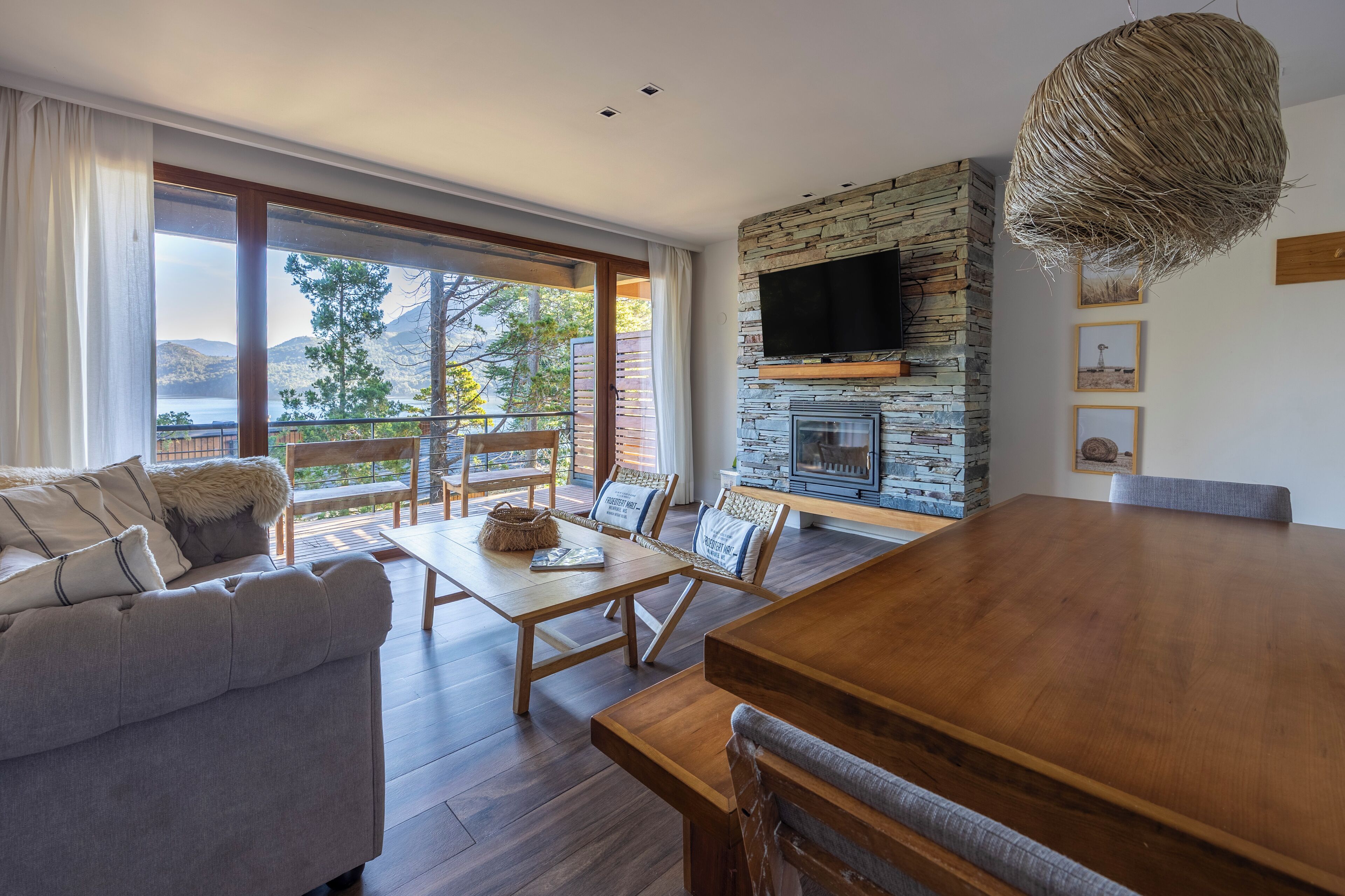 A modern living room with a stone fireplace, a large TV, and a dining area with a wooden table and chairs.