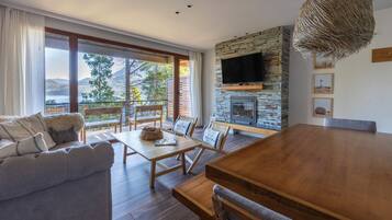 A modern living room with a stone fireplace, a large TV, and a dining area with a wooden table and chairs.