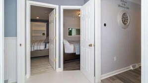 A hallway with two open doors leading to bedrooms. One room has a bed with a striped blanket, and the other has a bed with a white blanket. A clock is mounted on the wall in the hallway. - Seasonal Heated pool in the Bluegrass (Union)