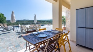 Terraço com mesa posta para refeições, cadeiras de exterior, guarda-sóis e piscina de pedra.