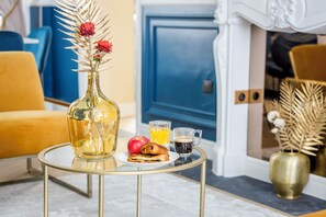 A dining table with a bottle, a plate with pastries, a glass of orange juice, and a mug of coffee in a room with blue and yellow decor.
