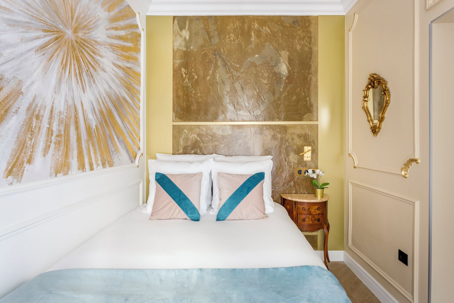 A neatly arranged bedroom with a bed, a wall-mounted mirror, and a decorative wall piece.