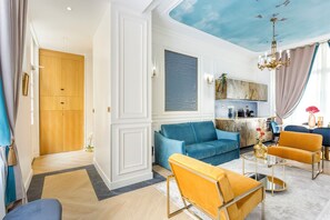 A modern living room with a blue sofa, yellow armchairs, and a kitchen area with a marble backsplash.