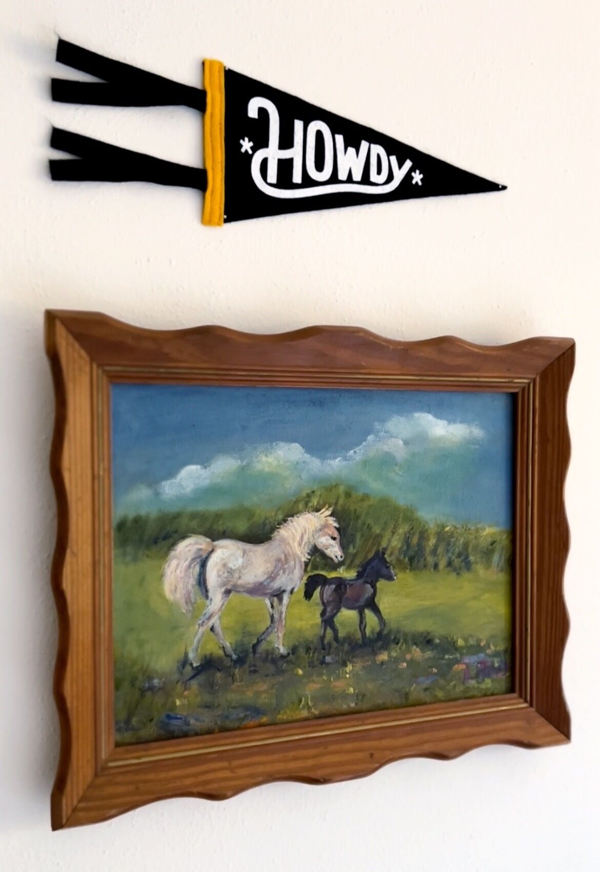 A framed painting of two horses in a field, with a banner above it that reads 'HOWDY'.