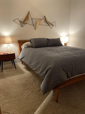 Contemporary bedroom with a neatly made bed, wooden headboard, and geometric wall art.