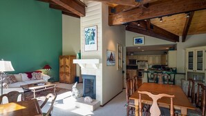 Amplia sala de estar con chimenea, vigas de madera y comedor con sillas y una mesa.