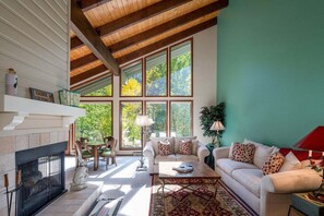 A spacious living room with a fireplace, large windows, a dining area, and a cozy seating arrangement. - Creek Front Duplex | Close to Lifts with Hot Tub (Ketchum)