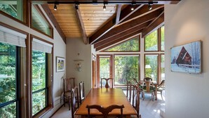 Un comedor con una larga mesa de madera y sillas, ventanas amplias y un techo alto con vigas a la vista.