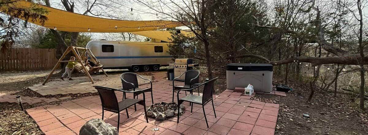 Een terras met tuinmeubilair, een schommelset, een barbecue en een mobiel toilet.