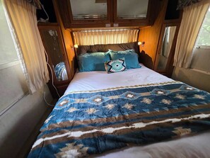 A bed with a patterned bedspread, a headboard with built-in lighting, and curtains on the windows.