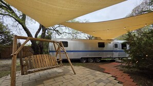 A patio with a swing set and a covered area, a trailer, and a brick pathway. - Airstream w flush toilet, city water, hot tub (Comanche County)