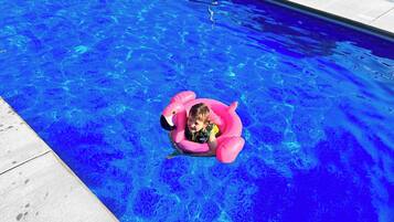 A child in a pink inflatable pool float in a clear blue pool.